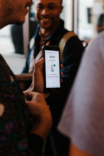 A customer holding up a phone showing the Augustin payment screen while buying a newspaper on the street
