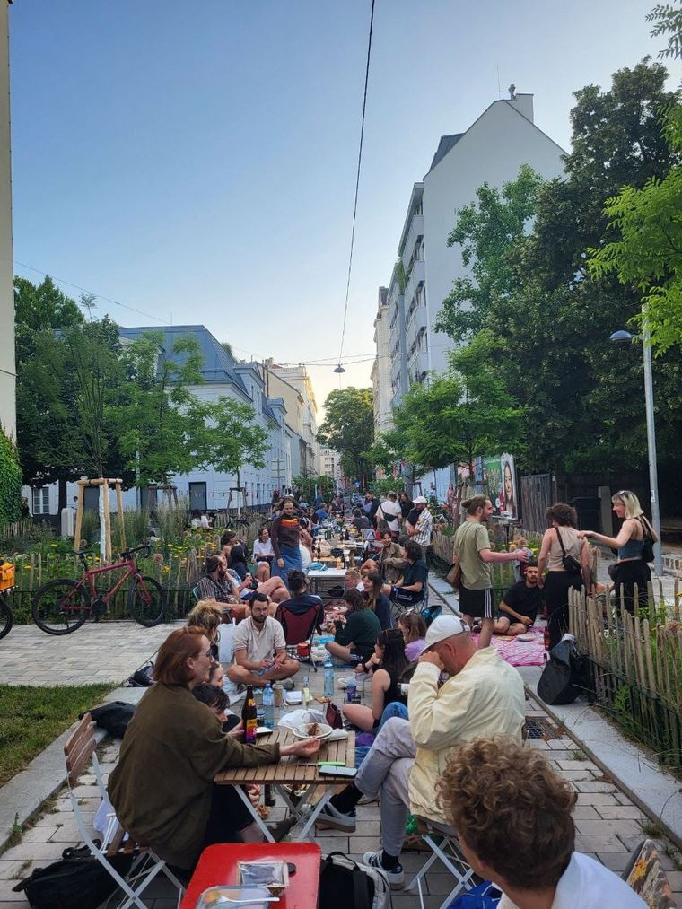 Neighbours sitting at tables and on blankets along a car-free Viennese street on a summer evening